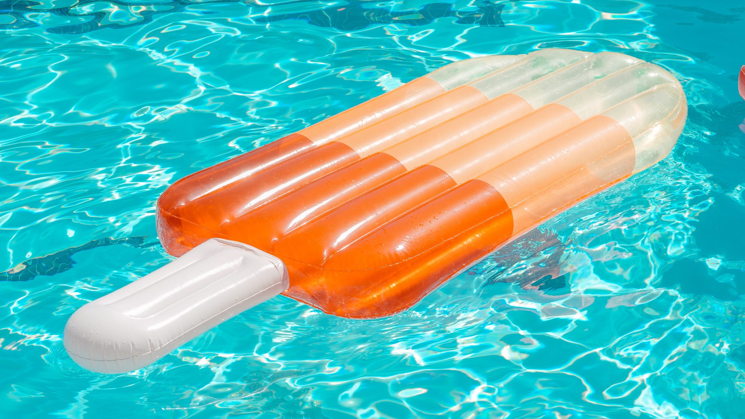 An orange popsicle shaped pool float, floating in a pool. This picture represents summer. 